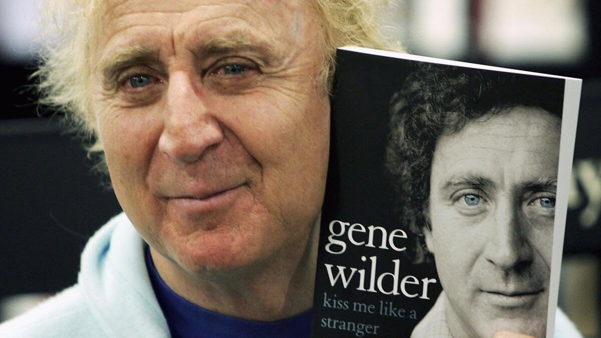 Gene Wilder holding his memoir Kiss Me Like a Stranger, his face beside his own black-and-white portrait on the cover