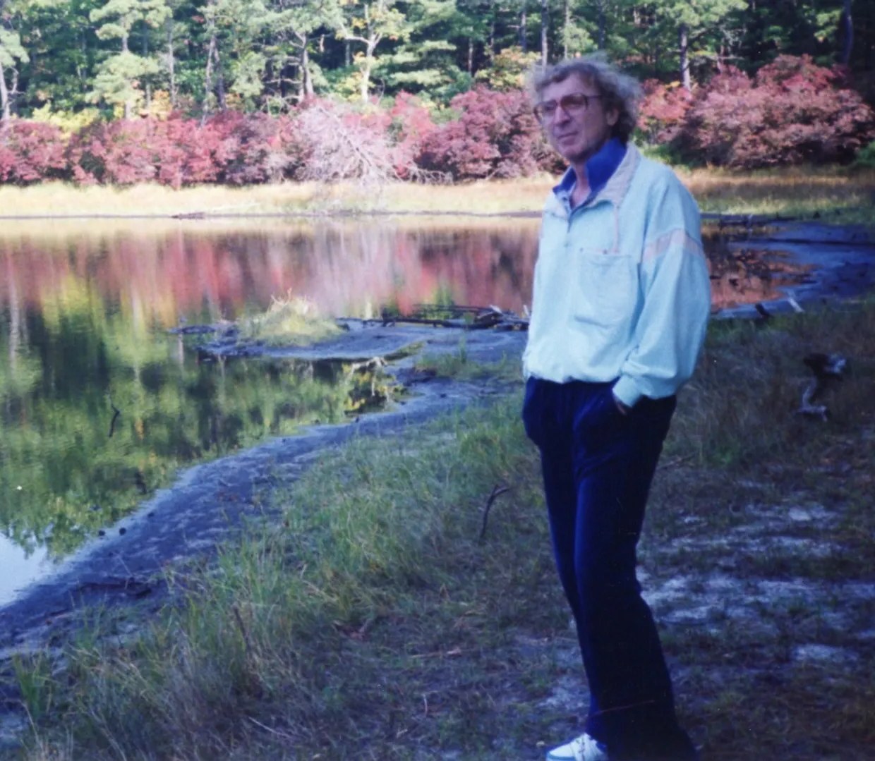 Gene Wilder standing by a still lake in autumn, quiet and reflective